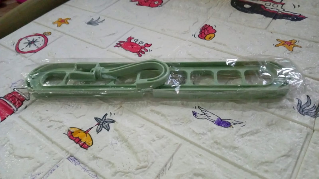 A green plastic multi-hole hanger in clear plastic packaging on a patterned surface.