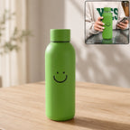 Green glass water bottle with a smiley face on a wooden table, with an inset showing a person holding a similar bottle.