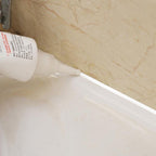 Close-up of white sealant being applied from a tube to a corner between a white surface and marble wall.