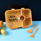 Closed yellow 4-compartment lunch box with clear lid and orange cutlery, on a blue surface with a flower.