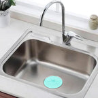 A light blue silicone drain strainer is placed in a clean stainless steel kitchen sink with a chrome faucet.