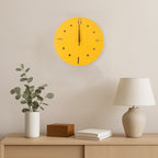 A yellow round wall clock hangs above a wooden console table with a plant, a wooden box, and a lamp.