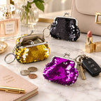Three sequined coin purse keychains in gold, black, and purple on a marble vanity, one holding coins and a key fob.