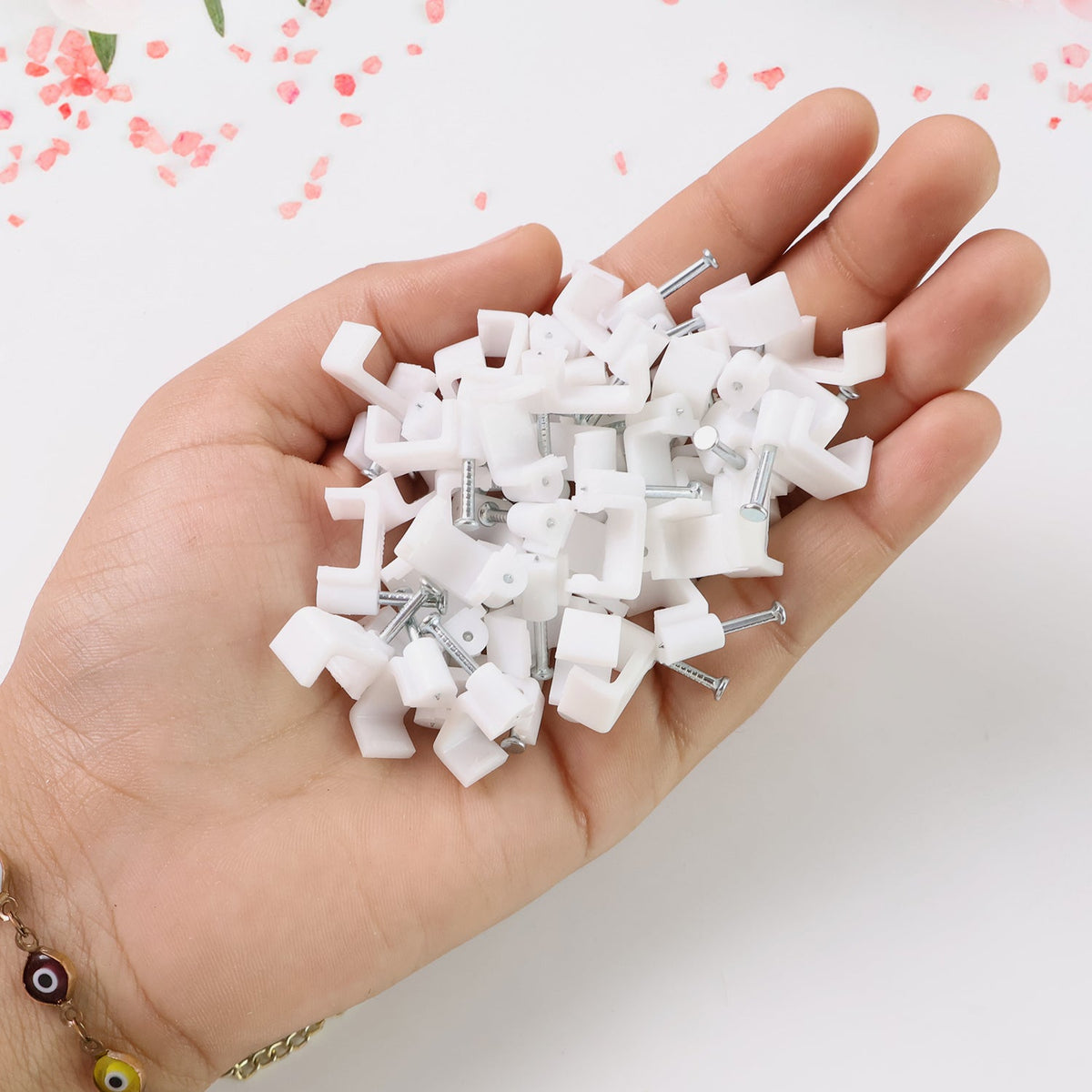 A hand holding a pile of white plastic cable clips with nails.