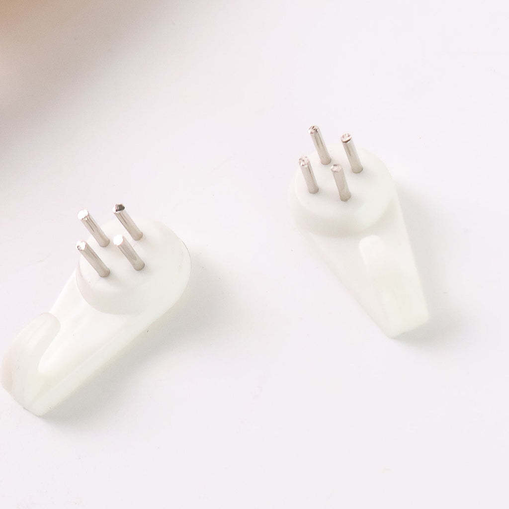 Two white plastic wall hooks with three metal pins each are shown on a white surface.