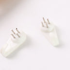 Two white plastic wall hooks with three metal pins each are shown on a white surface.