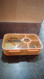 Closed yellow 4-compartment lunch box with clear lid and orange accents on a dark surface.