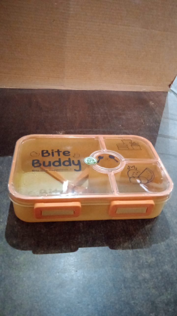 Closed yellow 4-compartment lunch box with clear lid and orange accents on a dark surface.