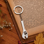 A silver metal mini adjustable wrench keychain lies on an open book with aged pages and small dried flowers.