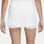 A woman models a white layered hip skirt with shorts and dark blue slip-on shoes, showing the back view.