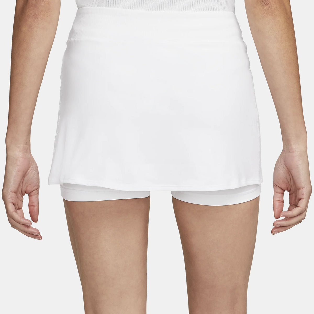 A woman models a white layered hip skirt with shorts and dark blue slip-on shoes, showing the back view.
