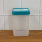 Empty clear plastic food storage container with a teal lid on a wooden surface against a white tiled wall.