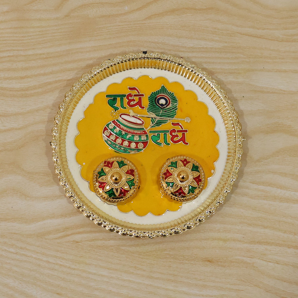 A silver and yellow Radhe Radhe pooja thali set with two small decorative containers on a light wooden background.
