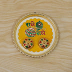 A silver and yellow Radhe Radhe pooja thali set with two small decorative containers on a light wooden background.