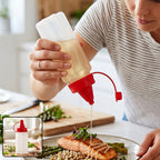 A person drizzles oil from a clear plastic squeeze bottle with a red cap onto salmon and asparagus. – view 8