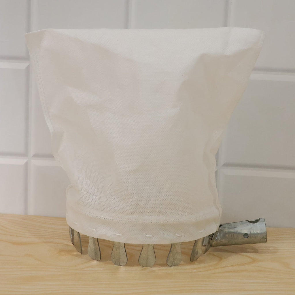 The white collection bag and metal prongs of the fruit picker are on a light wooden surface against a white tiled background.