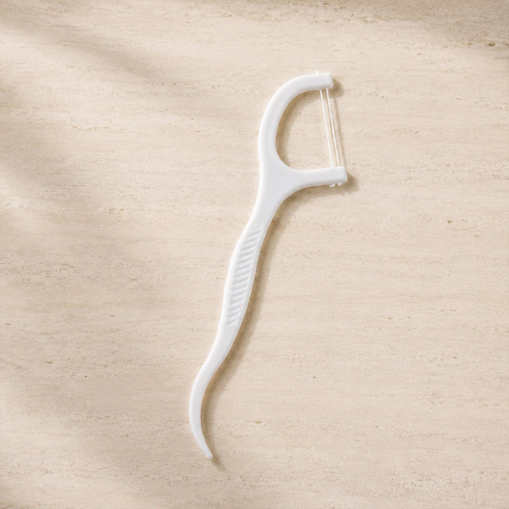 A single white dental floss pick with a textured handle lies on a light brown, textured surface.