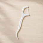 A single white dental floss pick with a textured handle lies on a light brown, textured surface.