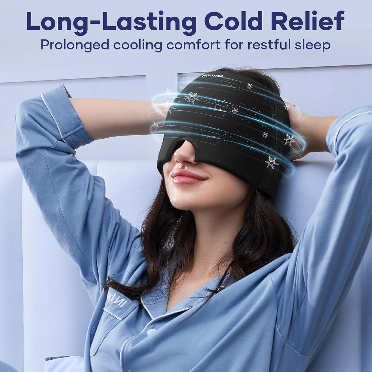 A woman in blue pajamas wearing a black migraine relief cap with blue cooling effects around her head.