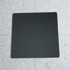 A square mirror with rounded corners lies flat on a speckled gray and white tiled floor.