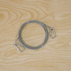 A coiled silver wire rope with two attached locking hooks on a light wooden background.