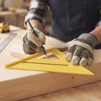 Gloved hands use a yellow plastic speed square and pencil to mark a piece of light wood.