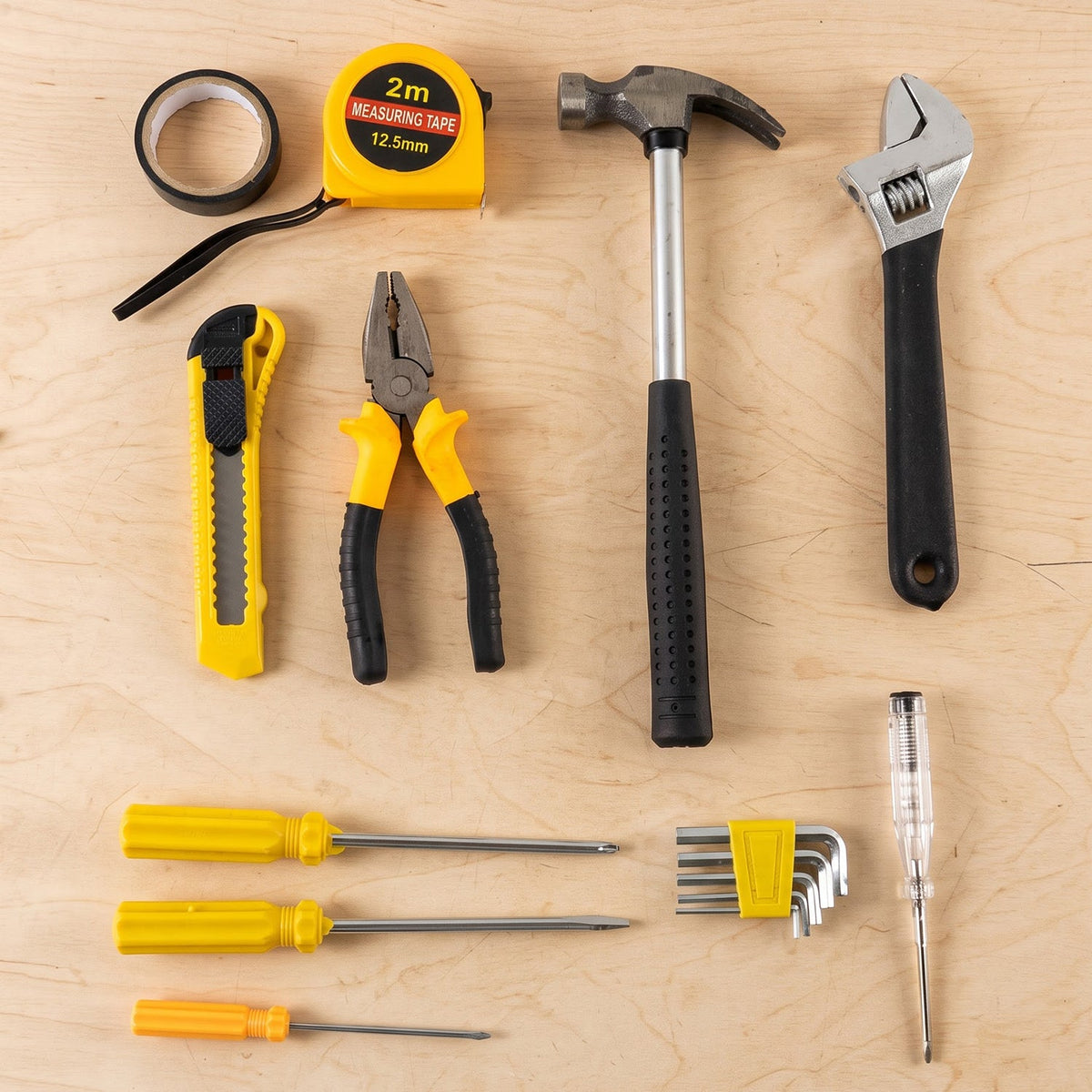 A flat lay of various hand tools on a light wooden surface, including a hammer, tape measure, pliers, and screwdrivers.