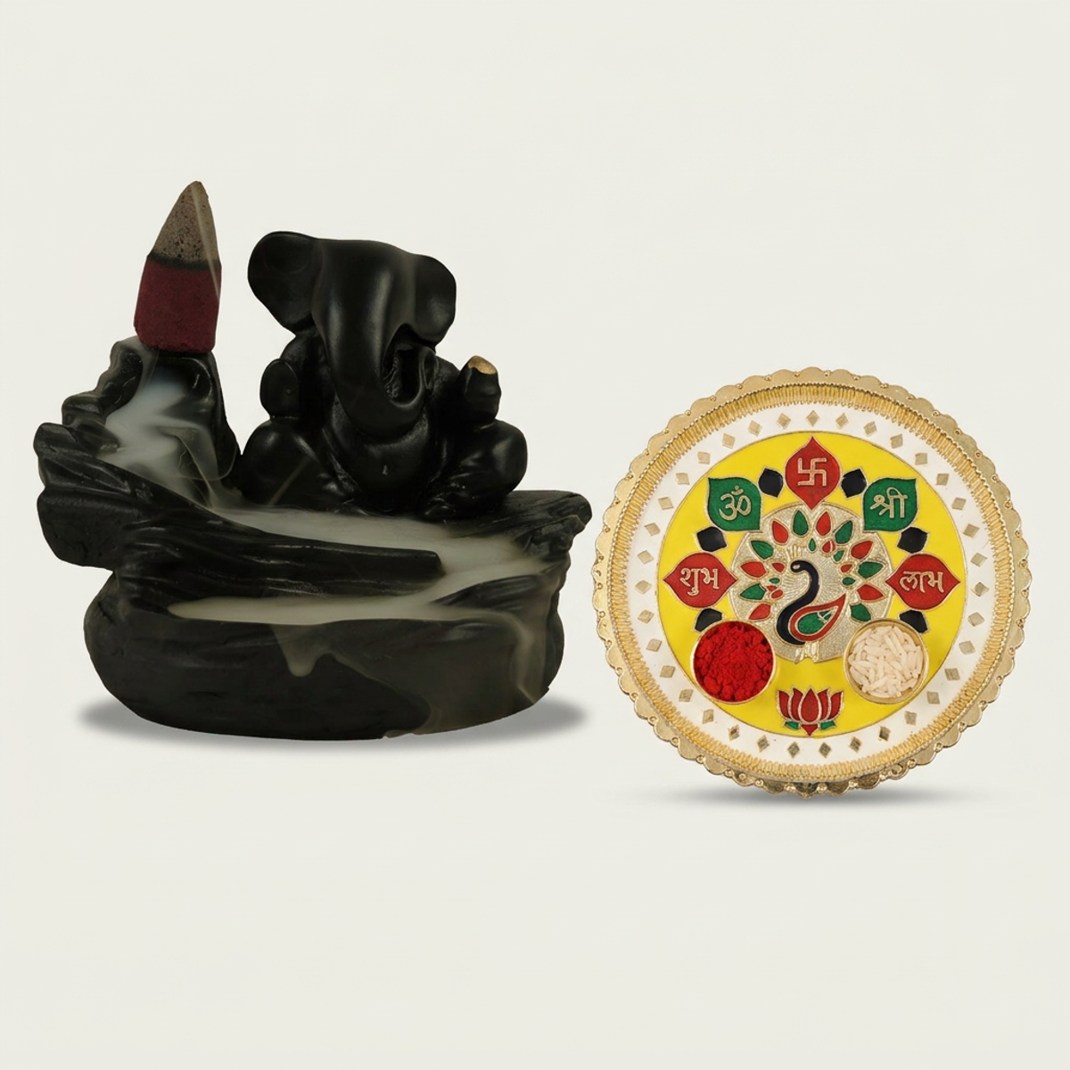 A black Ganesha backflow incense burner with smoke and a yellow and gold puja thali with peacock design on a white