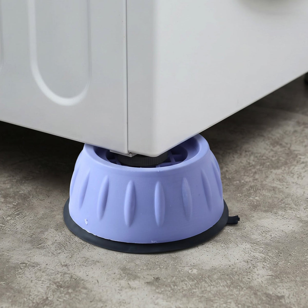 A washing machine elevated by a single purple anti-vibration pad on a tiled floor.
