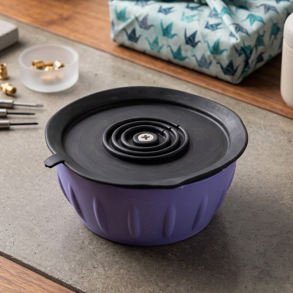 A purple anti-vibration pad with a black top featuring a spiral design and a screw, on a concrete surface.