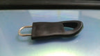 A black rubber zipper pull tab with a silver metal loop is placed on a shiny blue-grey surface.