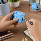 A person sharpening a green pencil with a light blue train-shaped double-hole pencil sharpener on a wooden desk.