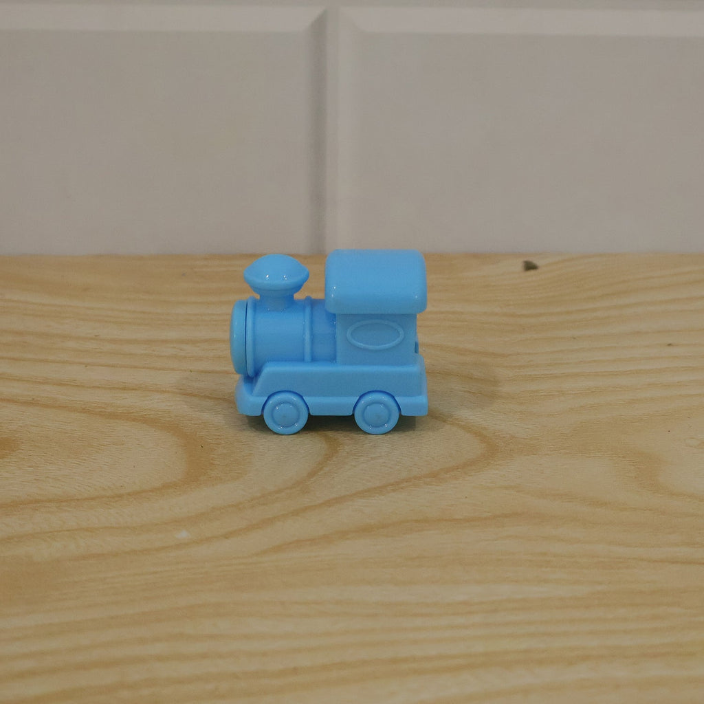 A light blue plastic train-shaped pencil sharpener resting on a light brown wooden surface with a white tiled background.