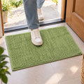 A person's feet in white sneakers stepping onto a bright green bobble mat placed on a tiled floor near a doorway.