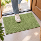 A person's feet in white sneakers stepping onto a bright green bobble mat placed on a tiled floor near a doorway.