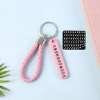 A pink braided wrist loop keychain with a pink number tag and a sheet of number stickers on a light blue surface.