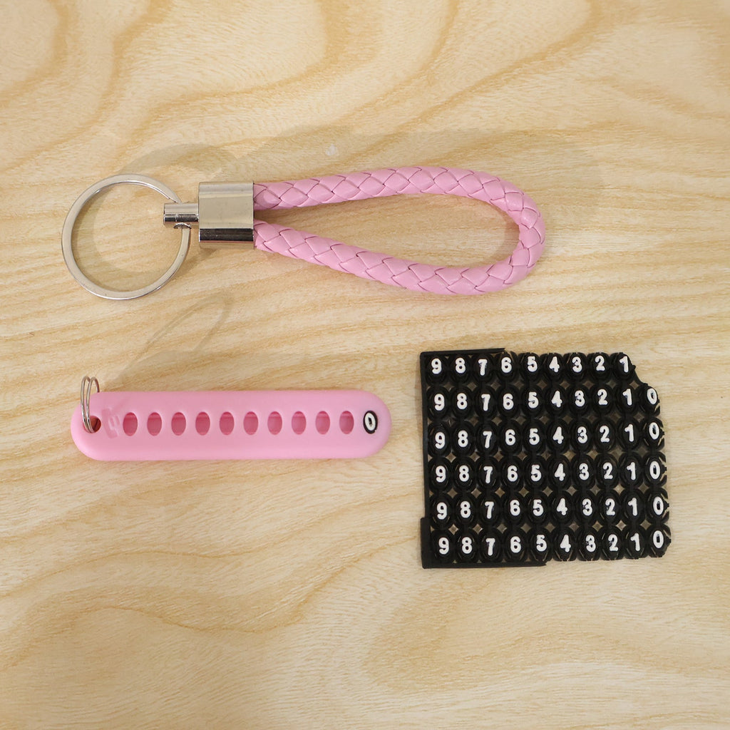A pink braided wrist loop keychain, a pink number tag, and a sheet of number stickers on a light wooden surface.