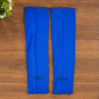 Two blue arm sleeves with the Ecoliz logo laid flat on a wooden surface next to a green plant.