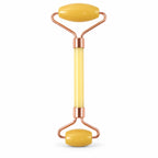 A yellow jade facial roller with rose gold colored metal accents is centered on a plain white background.