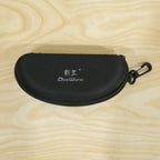 Closed black hard shell sunglasses case with a white logo and clip, on a light wooden surface.