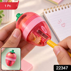A pink and red strawberry-shaped sharpener with a green stem is held, showing a yellow pencil being sharpened.