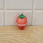 A pink and red strawberry-shaped sharpener with a green stem rests on a light wooden surface against white tiles.