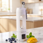 A white portable blender with a clear window and blades sits on a marble counter with blueberries, mint, and mango slices.