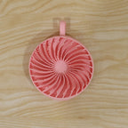 A pink silicone body scrubber with a spiral pattern of bristles and a hanging loop is centered on a light wooden surface.