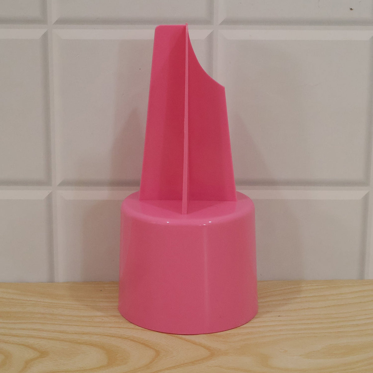 A pink plastic ground stake cup holder on a light wooden surface, with a white tiled wall in the background.