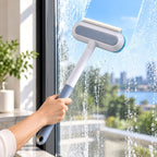A person's hand holds a long-handled window cleaner with a gray and white head, wiping a soapy window.
