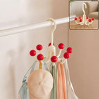 A cream multi-hook hanger with red ball tips, holding a light blue bag, a beige cap, and two scarves, hanging on a white rod.