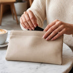 A woman's hands putting a black card into a cream textured faux leather pouch on a marble cafe table, with a coffee – view 3