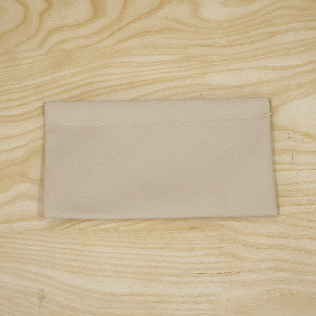 A cream textured faux leather pouch lying flat on a light wooden surface with visible grain.
