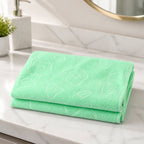 A folded light green microfiber towel with embossed patterns resting on a white marble bathroom counter.